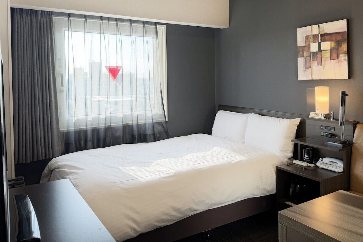 A hotel room with a bed, bedside table, lamp, and artwork on the wall.