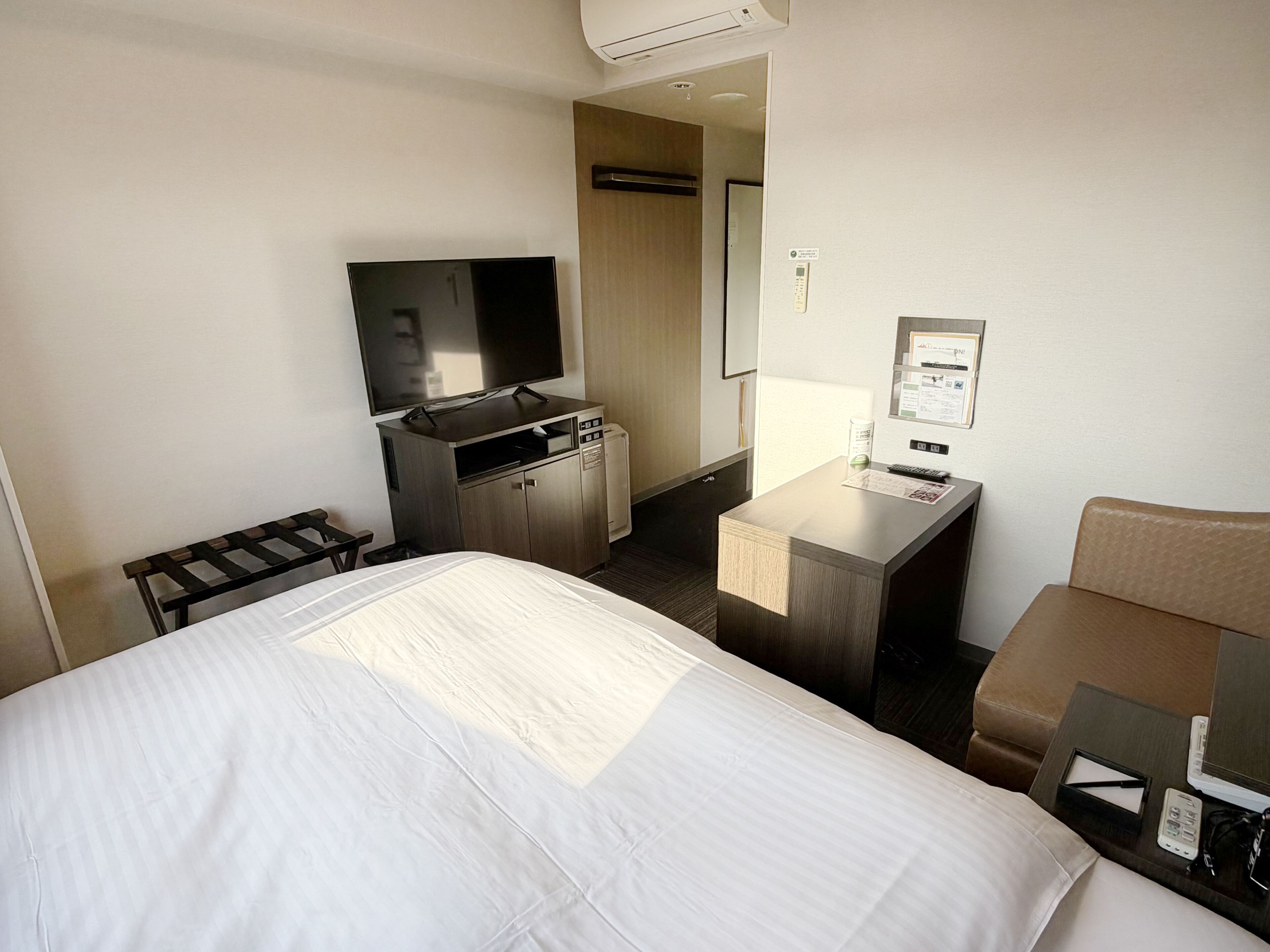 A hotel room with a bed, a desk with a computer, a TV, and a minibar.