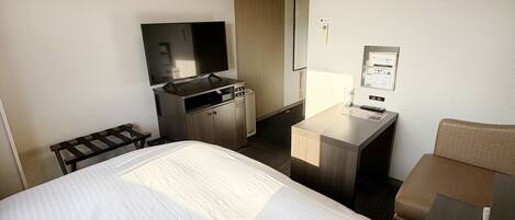 A hotel room with a bed, a desk with a computer, a TV, and a minibar.