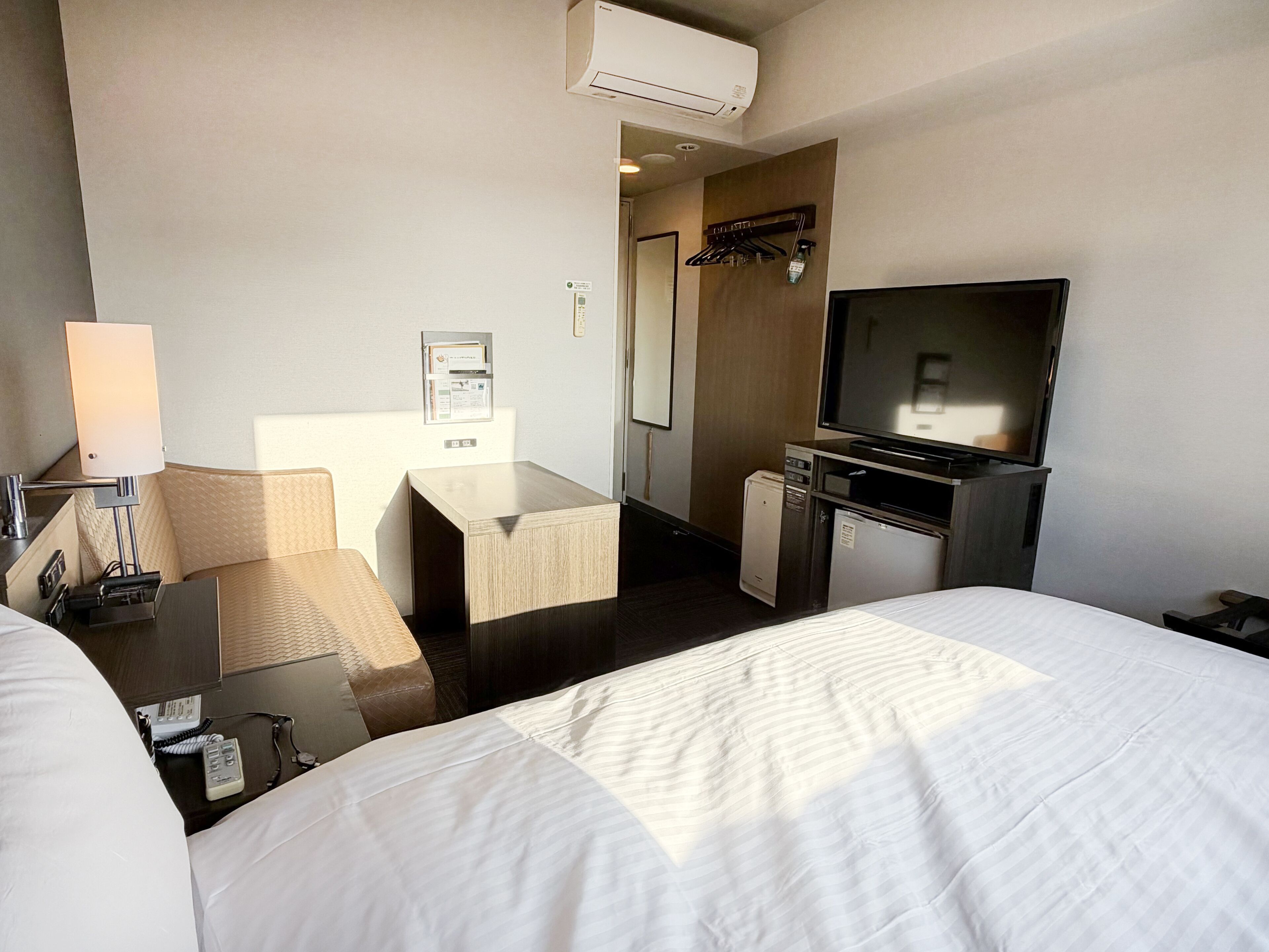Habitación de hotel con dos camas, un escritorio, televisión, minibar y aire acondicionado instalado en la pared.
