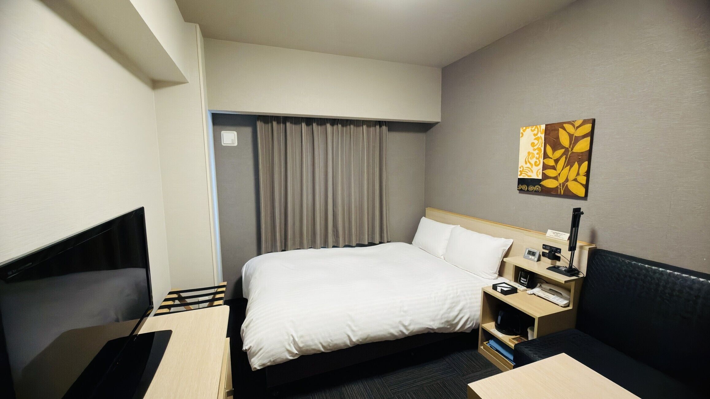 A hotel room with a bed, bedside table, lamp, and a painting on the wall.