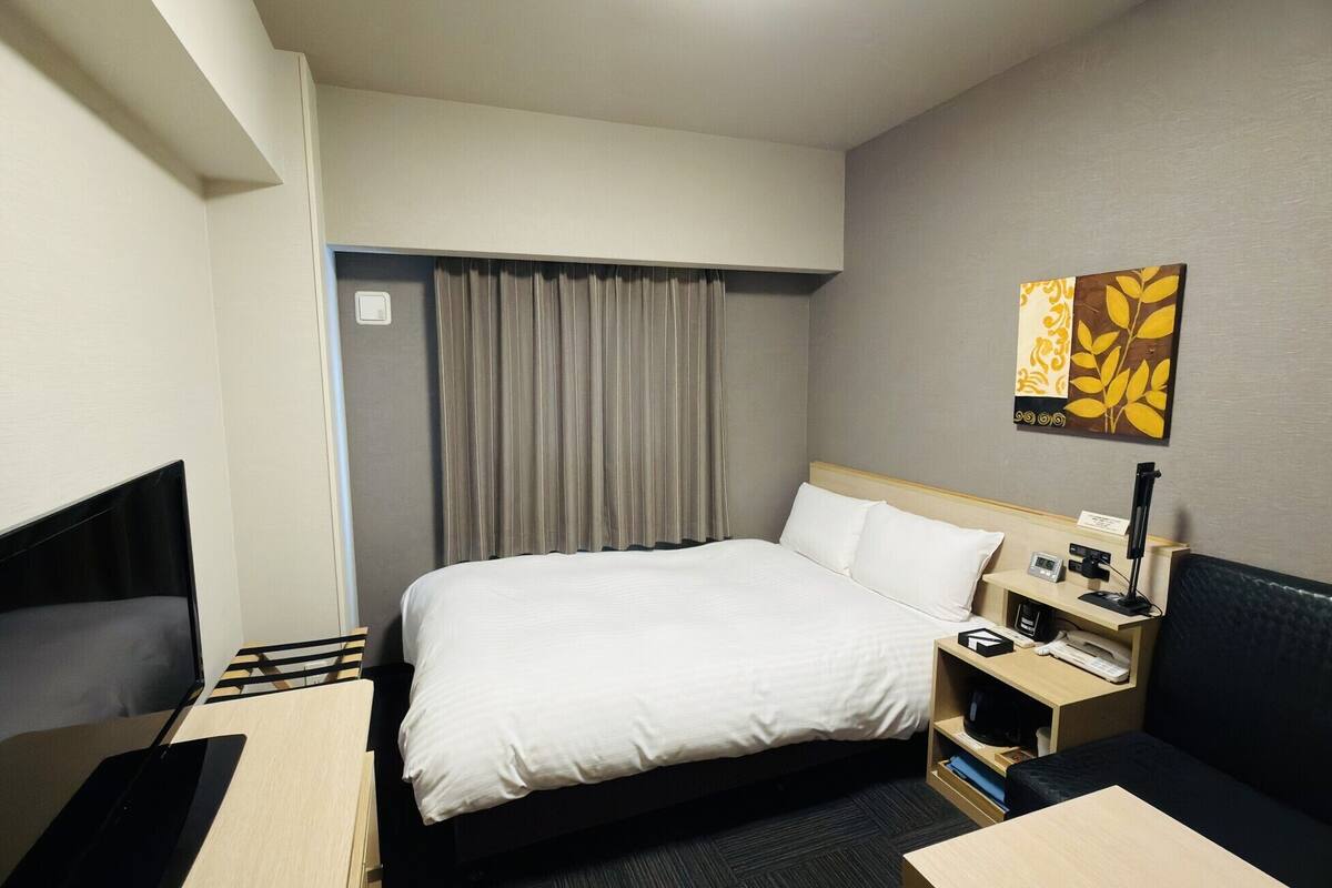 A hotel room with a bed, bedside table, lamp, and a painting on the wall.
