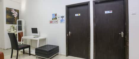 A room with a desk, computer, chair, ottoman, and two doors.