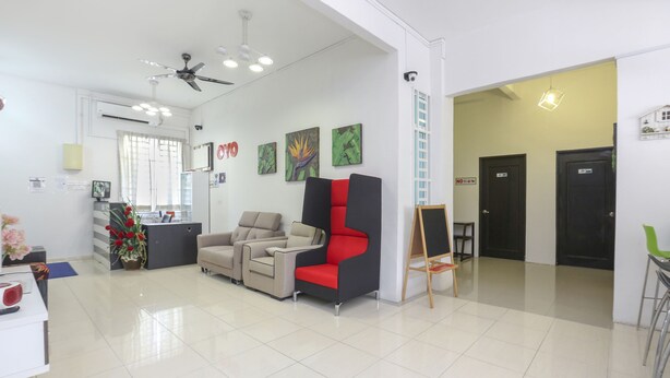 Un espace d’accueil moderne comprenant un comptoir de réception, un canapé, un fauteuil rouge et noir, et un tableau accroché au mur.