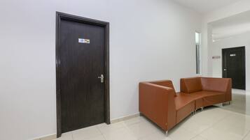 A hallway with a dark wooden door, a brown leather sofa, and a tiled floor.