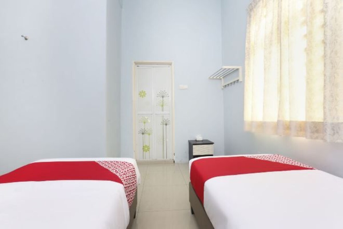 A room with two beds, a door, a small table, and a window with curtains.