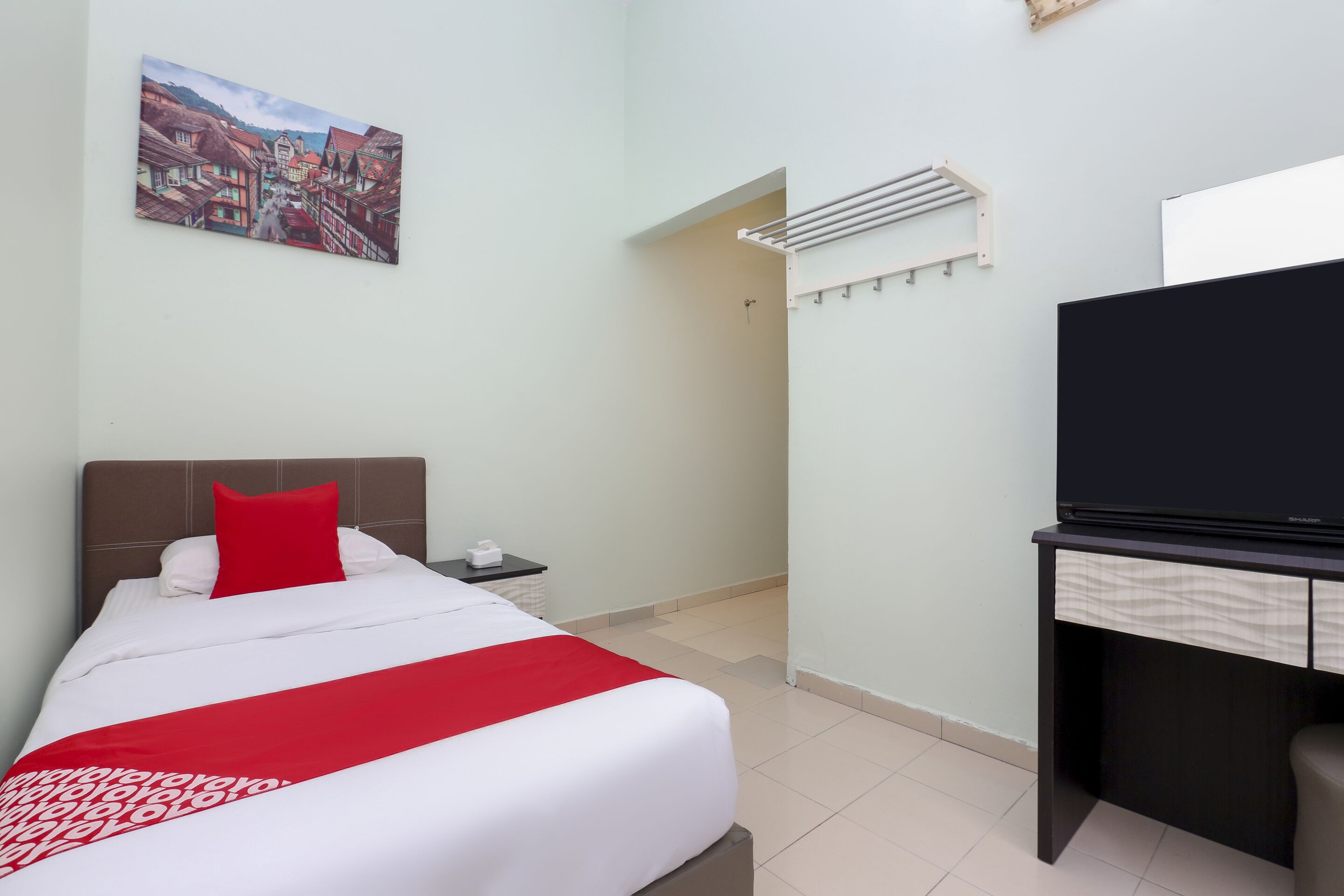 Ein Hotelzimmer mit Bett, Fernseher, Schreibtisch und einem Gemälde an der Wand.