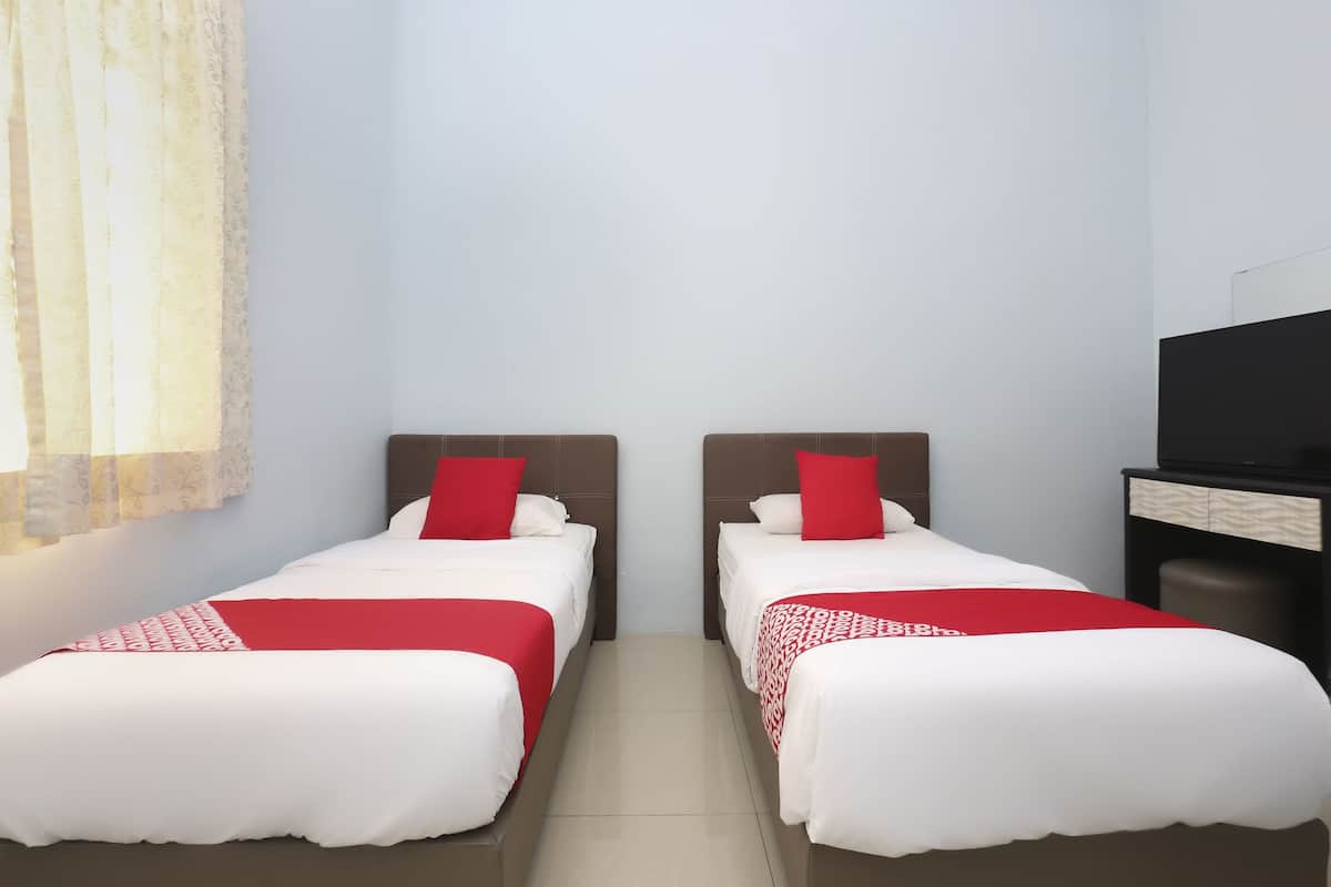 Habitación de hotel con dos camas individuales, cada una con cubrecama y almohadas rojas y blancas. A la derecha, hay un televisor sobre un soporte de madera.
