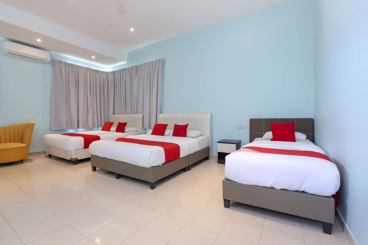 Habitación de hotel con tres camas, una silla y una mesita de noche.