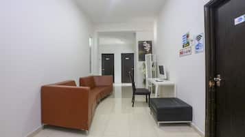 A hallway with a brown sofa, a black ottoman, a white desk with a computer, and a door with a Wi-Fi sign.