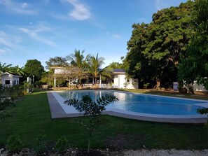 A swimming pool surrounded by a well-maintained lawn, with a house and trees in the background.