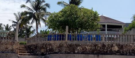 Una escalera de piedra conduce a un área cubierta con barandilla azul, palmeras y un edificio con tejado de azulejos.
