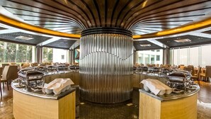A spacious buffet area with multiple serving stations, a central decorative column, and large windows providing natural light. - BCDM Rajendrapur (Pirozali)