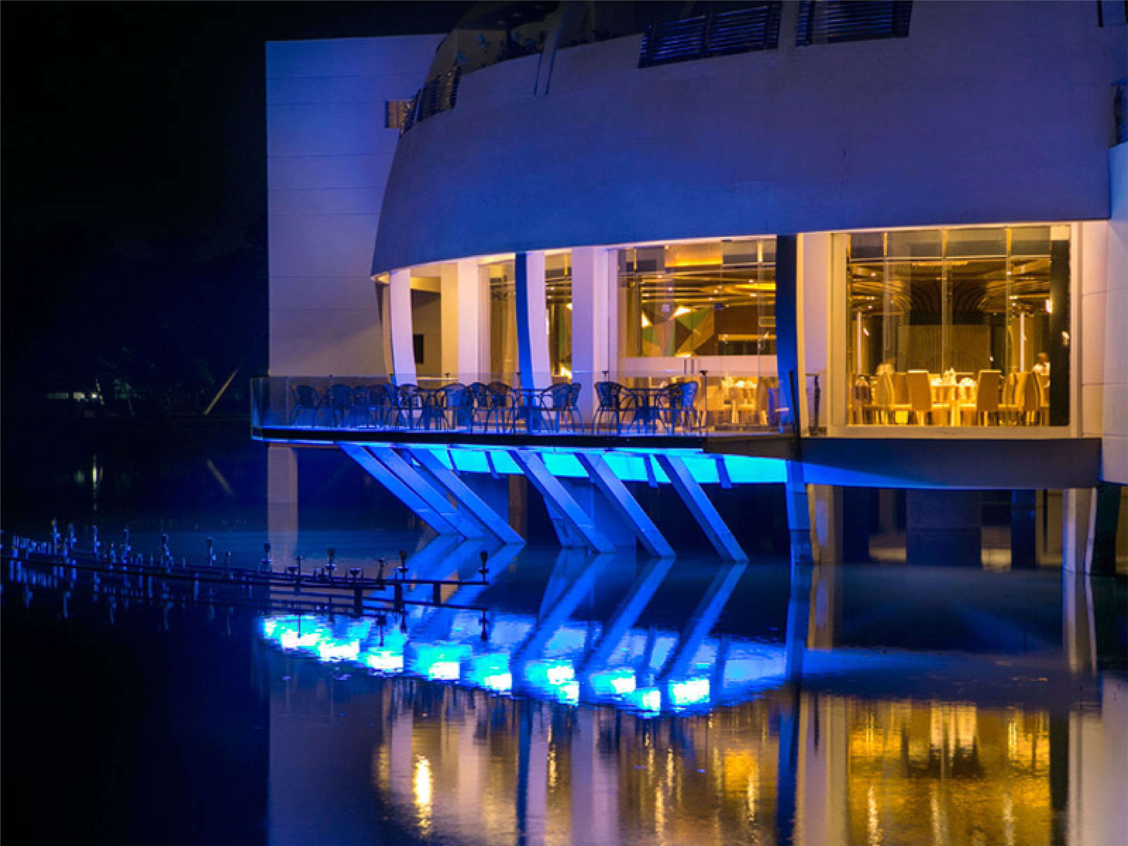 A modern building with a glass facade, a balcony, and a reflection in the water.