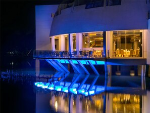 A modern building with a glass facade, a balcony, and a reflection in the water.