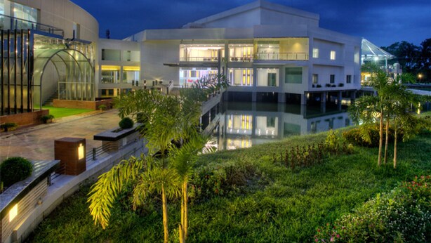 A modern building with a reflective pool, surrounded by greenery and a glass greenhouse structure. - BCDM Rajendrapur (Pirozali)