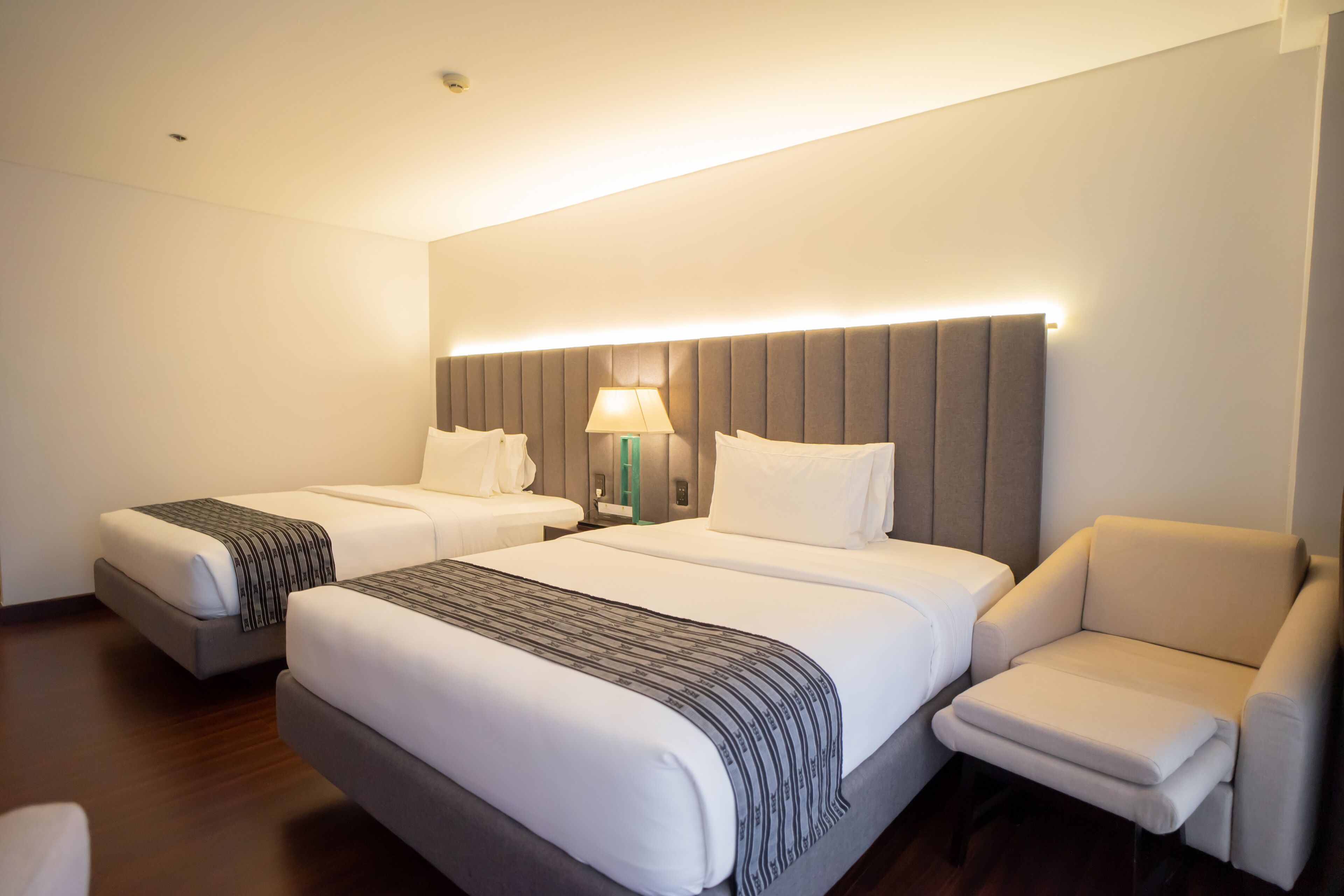 Une chambre d’hôtel avec deux lits, un canapé et une table de chevet avec une lampe.