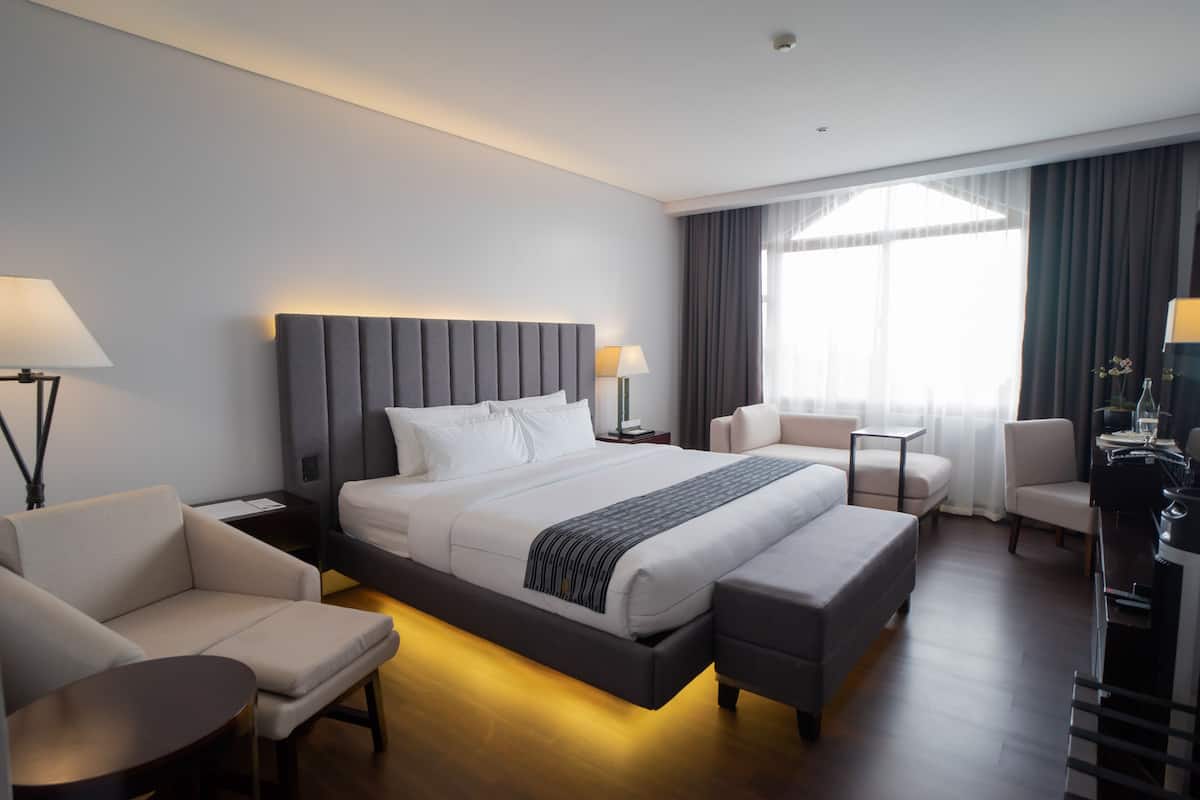 A modern hotel room with a large bed, a sofa, a desk, and a chair.