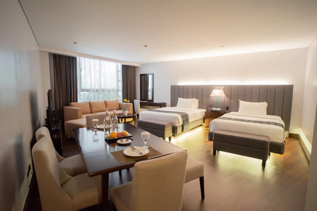 A hotel room with a dining area, two beds, a sofa, and a TV.