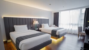 A modern hotel room with two beds, a desk, and a large window with curtains.