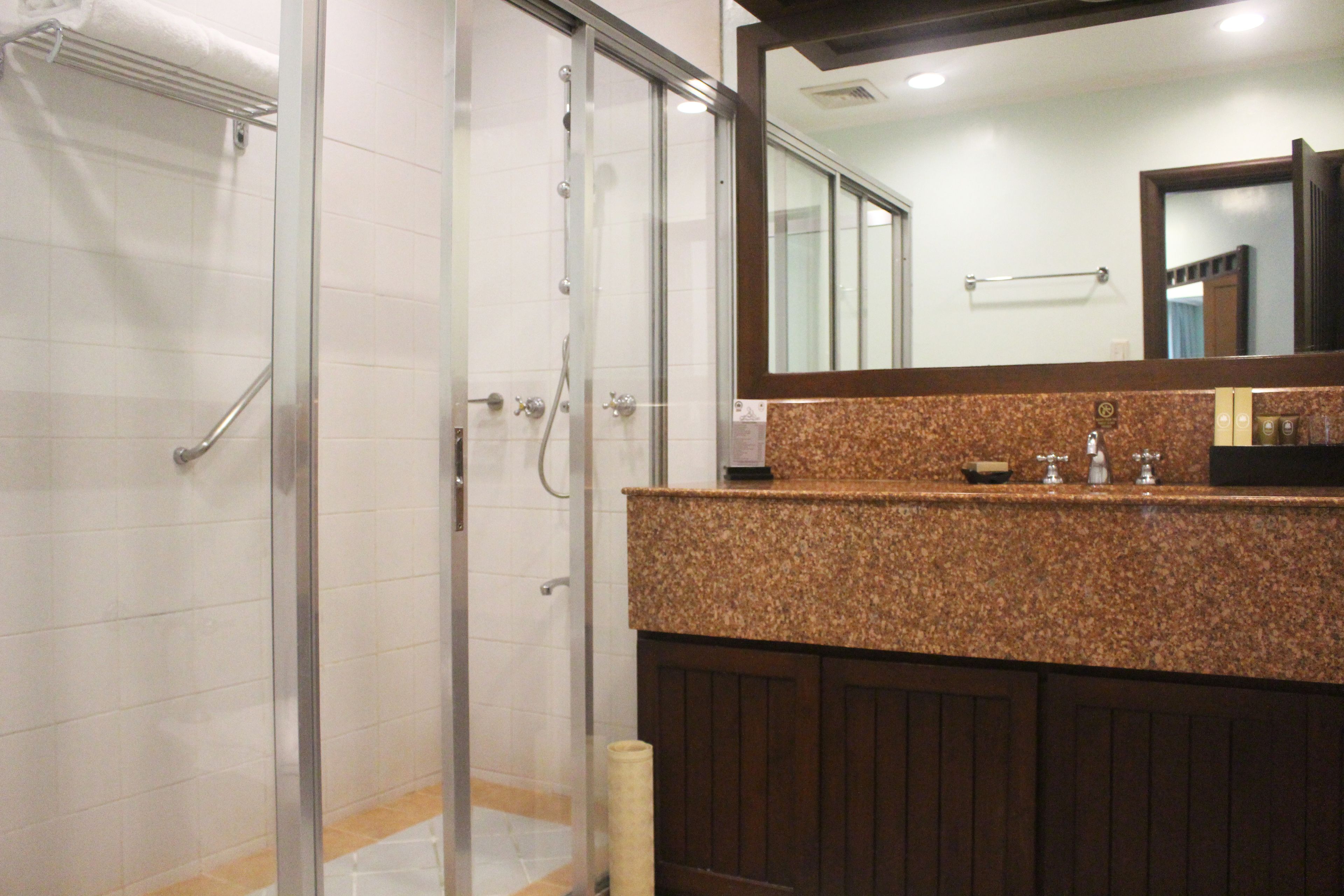 A bathroom with a glass shower enclosure, a granite countertop, and a wooden vanity.
