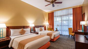 A hotel room with two beds, a desk, a chair, a ceiling fan, and a large window with curtains.