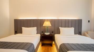 A hotel room with two beds, a nightstand with a lamp, and a wooden floor.