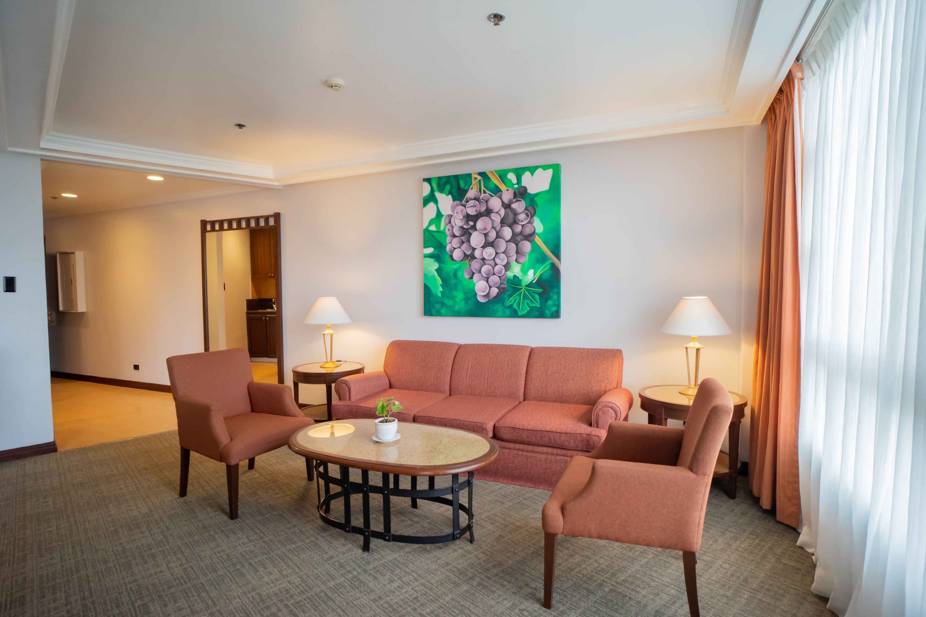A hotel room with a sofa, two armchairs, a coffee table, and a painting of grapes on the wall.