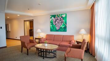 Habitación de hotel con sofá, dos sillones, una mesa de centro y un cuadro de uvas en la pared.