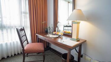 A hotel room with a wooden desk, a chair, a lamp, and a window with curtains.