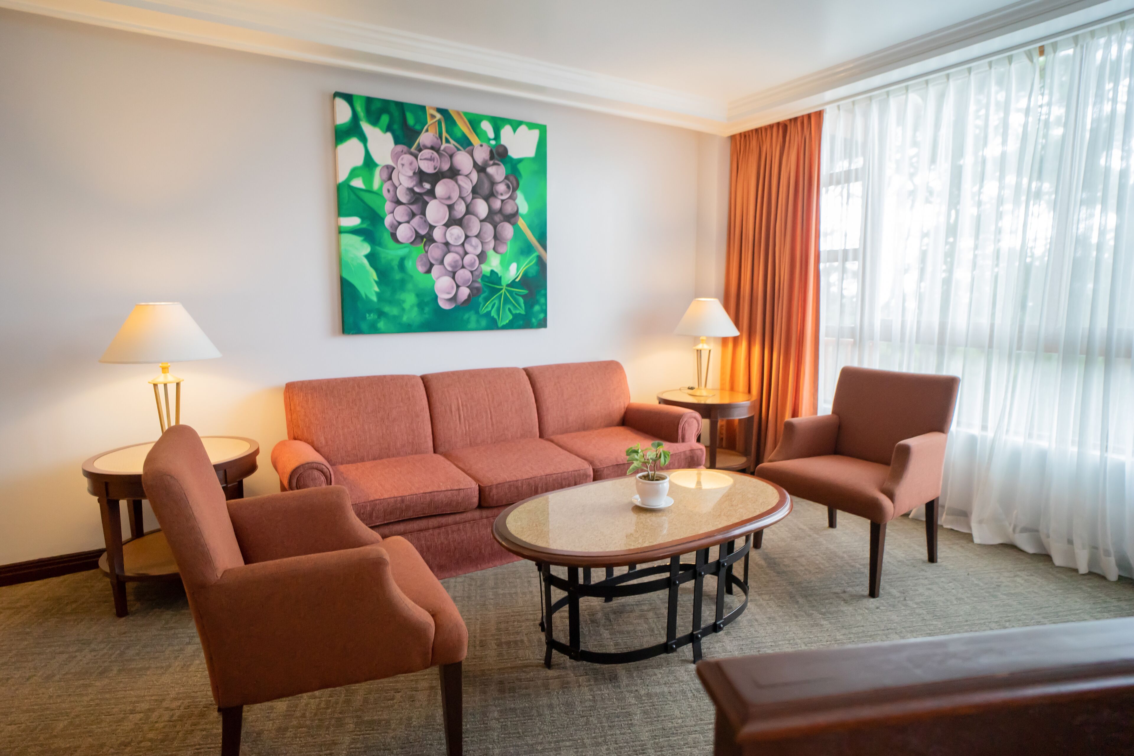 Una sala de estar con sofá, dos sillones, una mesa de centro y un cuadro de uvas en la pared.