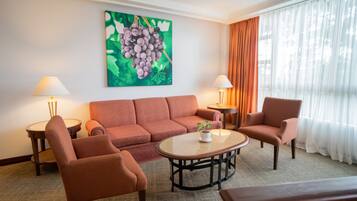 Una sala de estar con sofá, dos sillones, una mesa de centro y un cuadro de uvas en la pared.
