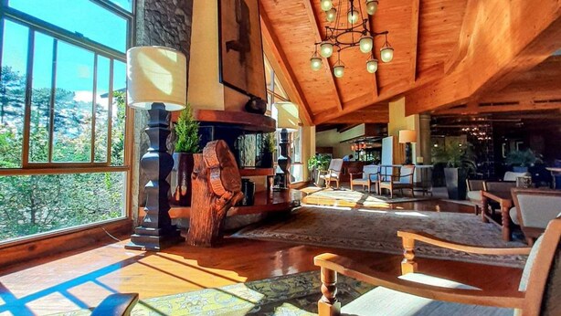 A spacious living area with wooden beams, a chandelier, and a large window offering a view of the outdoors.