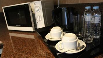 Una encimera de cocina con un microondas, dos tazas blancas con platillos, una cuchara y tres botellas de agua.