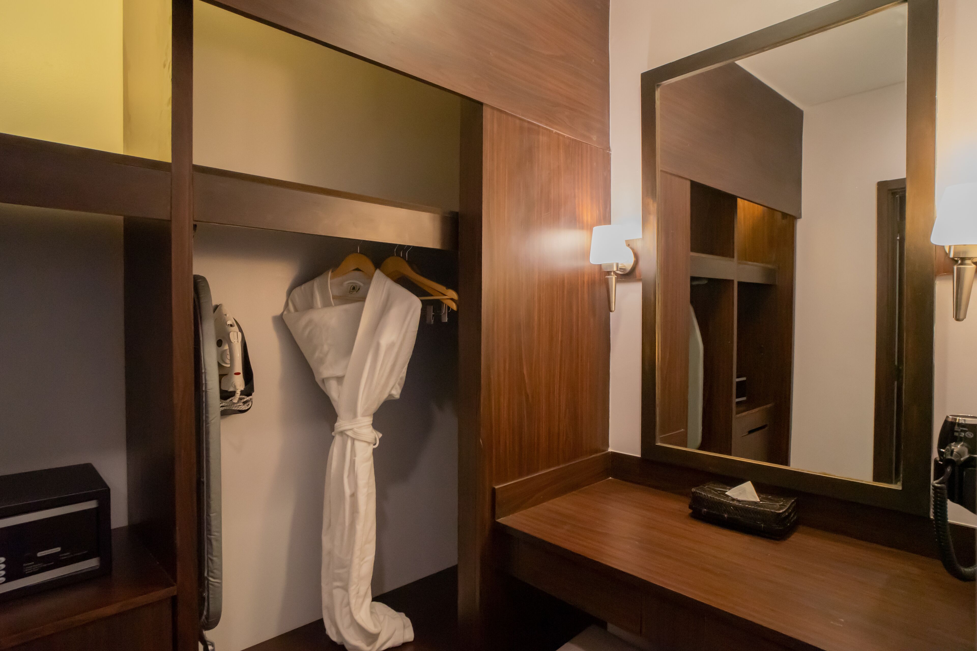 Et badeværelse på et hotel med en trækommode, en badekåbe hængende på væggen, et spejl og en telefon.