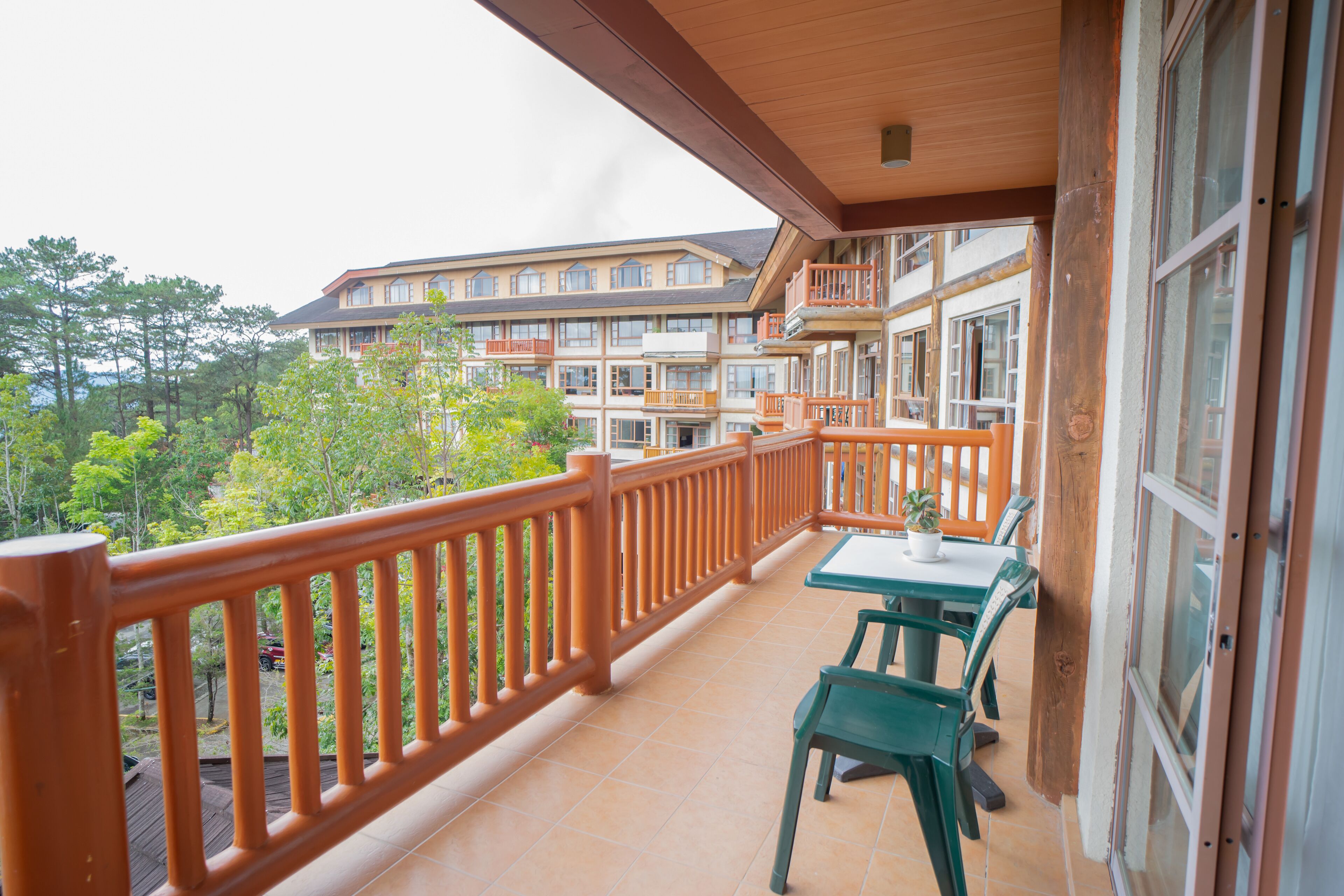 A balcony with a wooden railing, a table with chairs, and a view of a multi-story building with balconies.