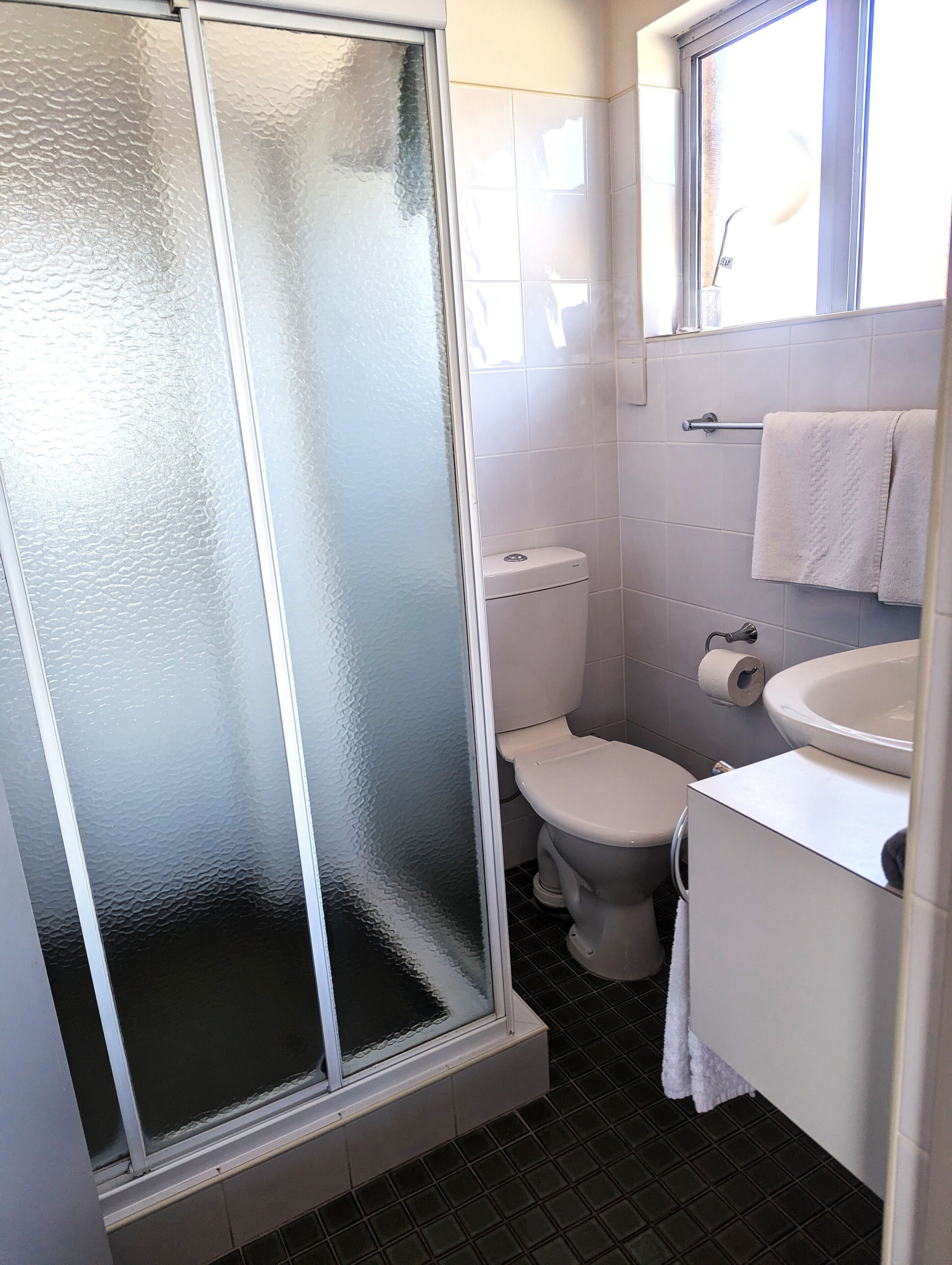 Un baño con cabina de ducha de vidrio, un inodoro y un lavabo con una toalla colgada en la pared.
