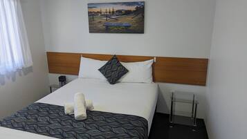 Habitación de hotel con cama, cabecero, mesita de noche, un cuadro colgado en la pared y una ventana con cortinas.