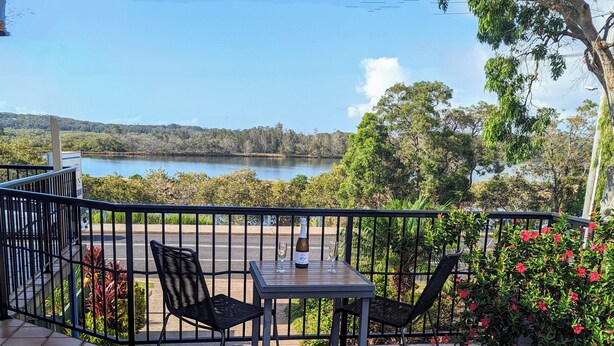 Una terraza con una mesa y sillas, una botella de vino y una copa, con vistas a un lago y vegetación.