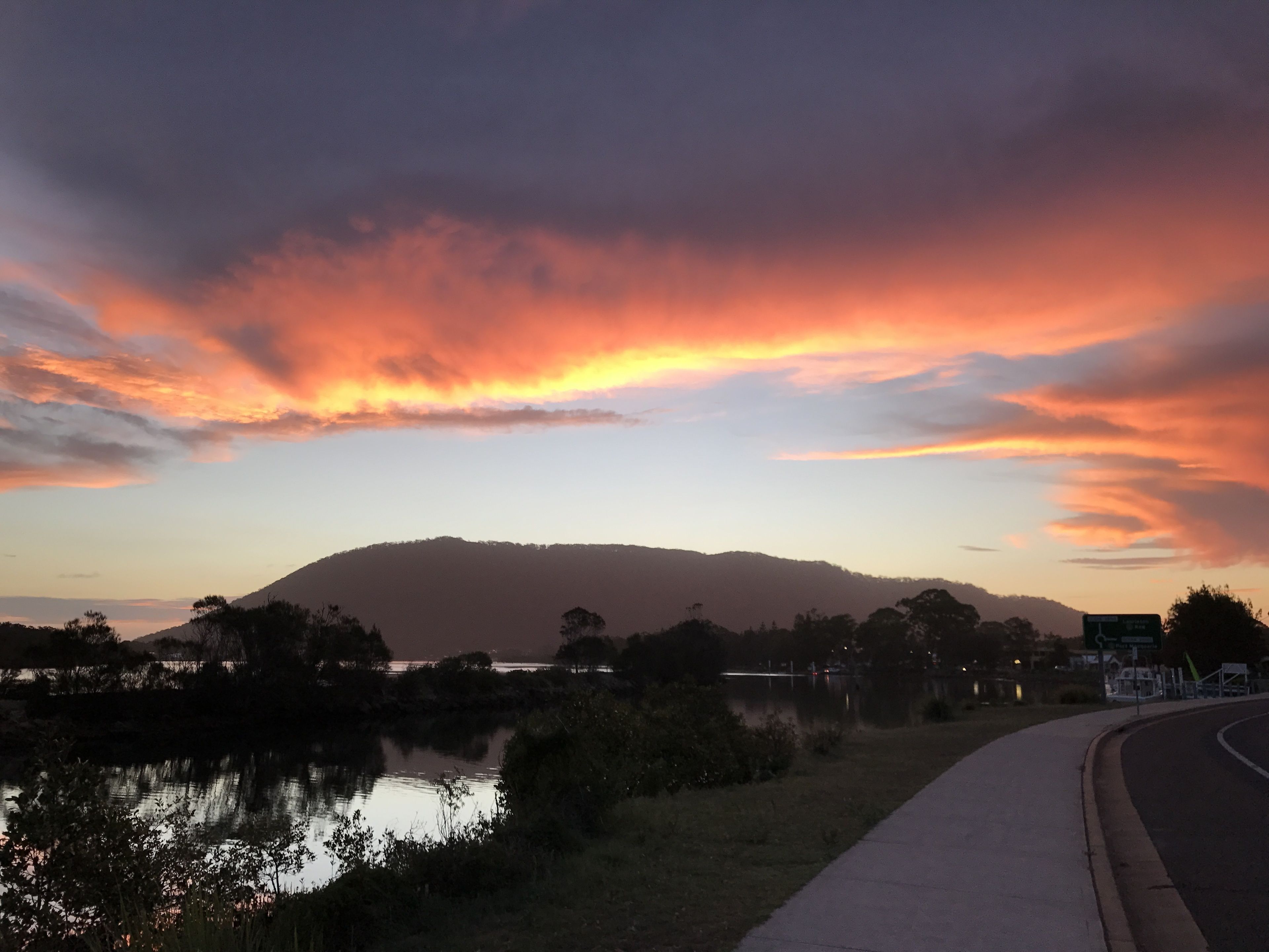 A sunset over a lake with a road curving to the right.