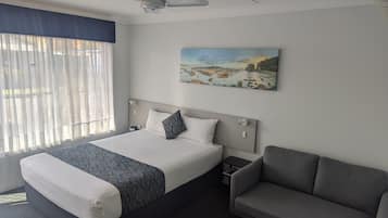 A hotel room with a bed, a gray sofa, a painting on the wall, and a ceiling fan.