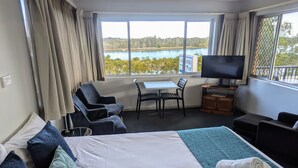 Habitación de hotel con cama, escritorio, silla, televisión y vista al lago.