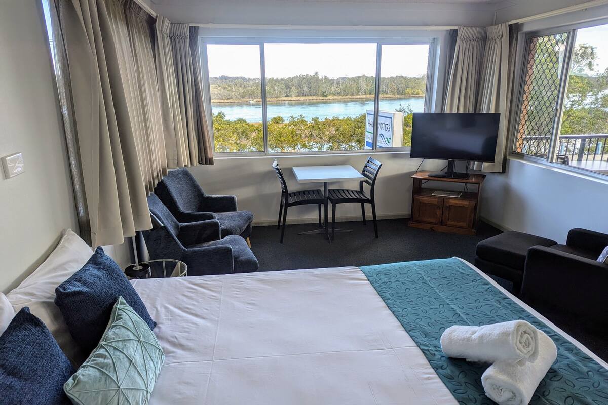 A hotel room with a bed, a desk, a chair, a TV, and a view of a lake.