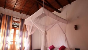 Ein Zimmer mit einem Bett unter einem Baldachin, einem kleinen Nachttisch und einem Fenster mit Vorhängen.