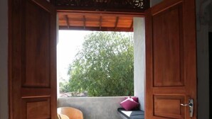 Eine Holztür führt zu einem Balkon mit einem Korbstuhl und einem rosafarbenen Kissen.