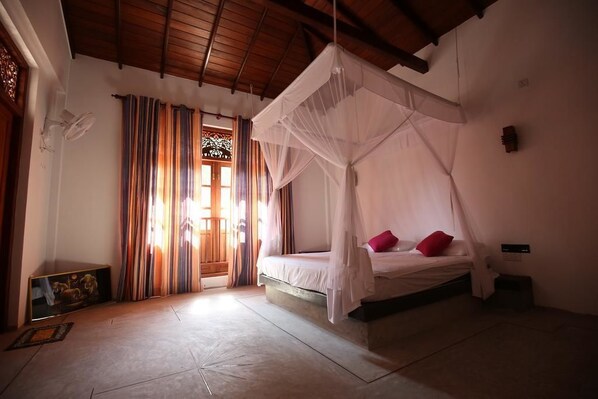 A room with a bed under a canopy, a window with curtains, and a small table with a picture.