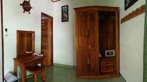 A room with a wooden desk, chair, and wardrobe, a trash bin, and a wall-mounted clock. - New Paradise Home Resort (Rayong)