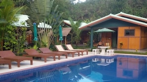 A pool area with lounge chairs and a small building with a green roof. - New Paradise Home Resort (Rayong)