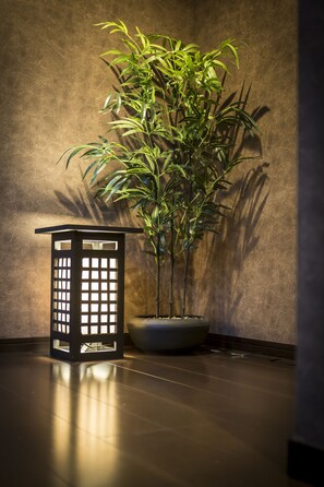 A potted bamboo plant next to a black lantern on a polished floor against a textured wall.