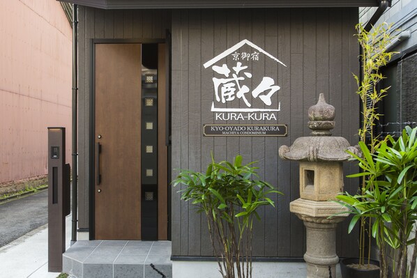 A building entrance with a sign reading "KURA-KURA" and "KYO-OYADO KURAKURA MACHIYA CONDOMINIUM".